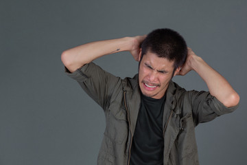 Short-haired man wearing a dark green shirt, angry temper stood on a gray background.