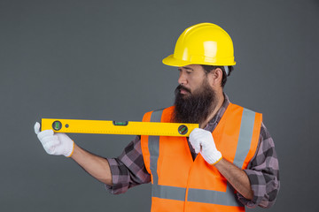 An engineering man wearing a yellow helmet holding a water level meter on a gray background.