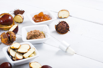 medicine cream, ground conkers tincture with alcohol and sliced seeds from horse chestnuts, on white wooden table