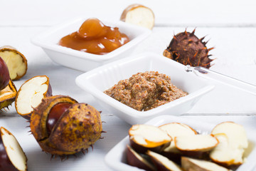 medicine cream, ground conkers tincture with alcohol and sliced seeds from horse chestnuts, on white wooden table