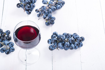 glass of red wine and blue grapes on white wooden table background