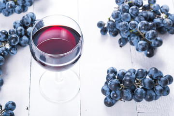 glass of red wine and blue grapes on white wooden table background