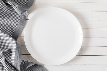 Empty white plate on wooden white table with checkered blue linen napkin. Flat lay, top view, copy...