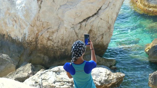 Young woman traveller standing on the rock and taking picture