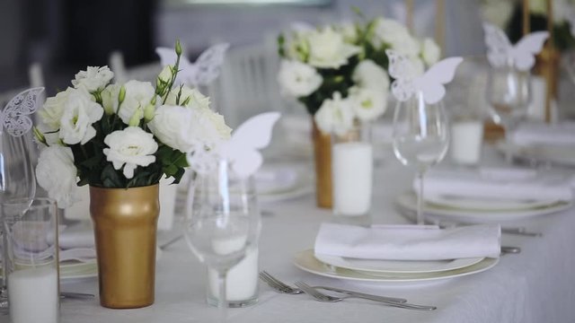 luxury white table decoration with flower bouquets and paper butterflies on wine glasses closeup slow motion