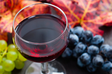 glass of red wine and grapes on black wooden table background