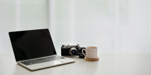 Open laptop computer with coffee cup and vintage camera on white table