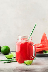 Freshly squeezed watermelon smoothie with lime in glass jar and slices of watermelon on gray kitchen table background