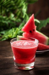 Freshly squeezed watermelon smoothie in glass and slices of watermelon on old wooden kitchen table background