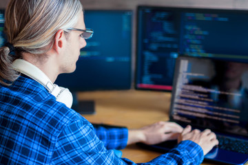Back view of man freelancer in white headphones is working at home office. Programmer developer is...