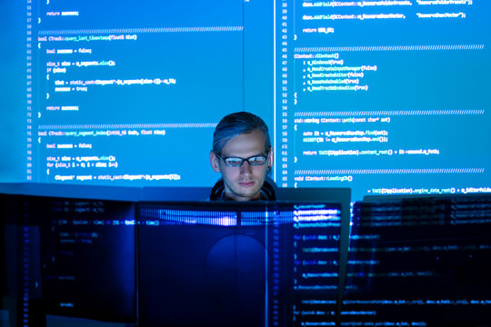 Software developer freelancer man male work with program code C++, Java, Javascript on wide displays at night. Develops new web desktop mobile application or framework. Projector futuristic background