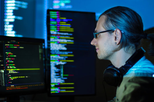 Software developer freelancer man male in headphones work with program code C++ Java Javascript on wide displays at night Develops new web desktop mobile application or framework. Projector background
