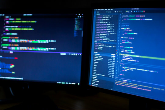 Modern blue wide displays, monitors of software developer with program code of application. Complex C++, Java, Javascript program code shows on displays. Freelancer software developer workplace.