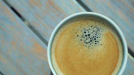 close up top view on cup of coffee wth foam on wooden surface