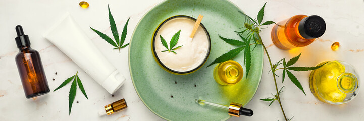 Bank of medicinal cream with CBD oil, bottle of cannabis oil, capsules, on a green plate. Flat lay,...
