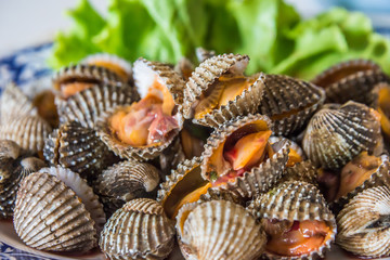 Steamed blanched cockles with Thai seafood dipping sauce and lettuce in the white dish.