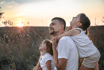 Dad and his daughters in the field at sunset .