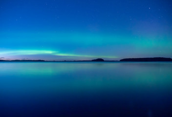 Naklejka na ściany i meble Northern lights dancing over calm lake in Farnebofjarden national park in Sweden.