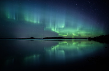 Northern lights dancing over calm lake in Farnebofjarden national park in Sweden.