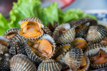 Steamed blanched cockles with Thai seafood dipping sauce and lettuce in the white dish.