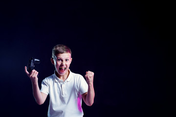 Naklejka premium Cheerful kid with open mouth and joystick shouting for joy after winning in video game on black background