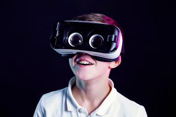 Side view of excited kid in white t-shirt and virtual reality headset standing bending forward...