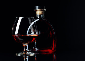 Glass and bottle of brandy on a black reflective background.