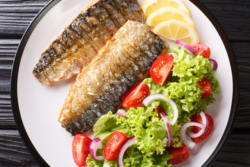 Diet healthy food grilled mackerel fillet with lemon and fresh vegetable salad close-up on a plate. Horizontal top view