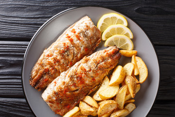 Grilled mackerel filet served with fried potatoes and lemon slices closeup on a plate. Horizontal top view