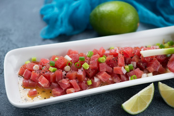 Tuna fillet ceviche served on a white plate, closeup on a blue stone background, selective focus