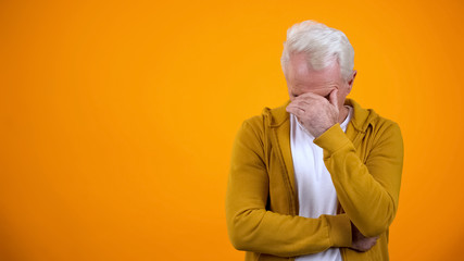 Dissatisfied retired man closing face with palm, failure concept, disappointment