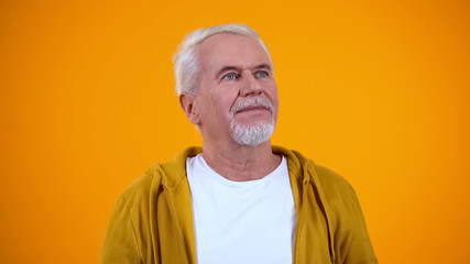 Thoughtful elderly male looking up, dreaming of good things, yellow background