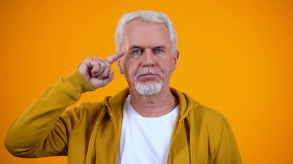 Serious retired male showing screw loose sign on camera, nonsense or absurd