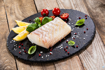 Fresh raw cod with herbs served on black stone on wooden table