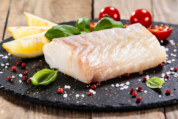 Fresh raw cod with herbs served on black stone on wooden table