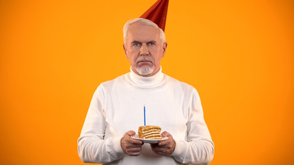Lonely senior male holding birthday cake, sadly looking at camera, solitude