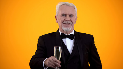 Smart senior gentleman in suit holding beverage glass and smiling, flirting