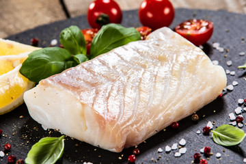 Fresh raw cod with herbs served on black stone on wooden table