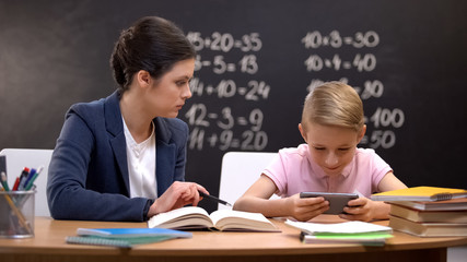 Unhappy teacher trying to explain task to boy playing on smartphone, disrespect