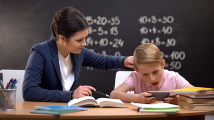 Irritated lady teacher grabbing boys playing on smartphone ear, punishment