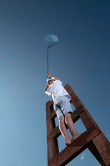 A little boy on a wooden staircase leading to the sky with butterfly net wants to catch something interesting 