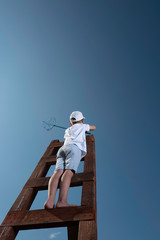 A little boy on a wooden staircase leading to the sky with butterfly net wants to catch something interesting 