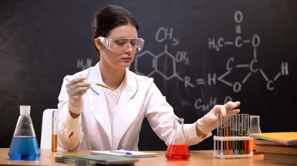 Woman scientist holding pipette with liquid and taking test tube with reagent