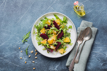 Beets, orange, pine nut, olive oil, feta cheese and arugula salad in ceramic plate on old concrete table background. Top view.