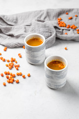 Hot sea buckthorn tea in a ceramic mug. Sea buckthorn berries are scattered on a white table.