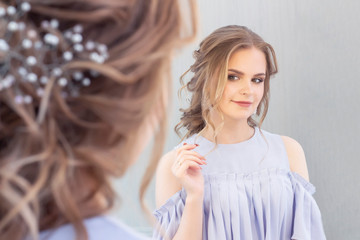 beautiful girl with a wedding hairstyle looks at herself in the mirror, portrait of a young girl. beautiful make-up. beauty saloon