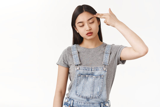 Bored Reluctant Asian Dark-haired Girl Cannot Stand Boring Talk Close Eyes Hold Finger Pistol Shoot Herself Commit Suicide Boredom Uninteresting Event Sighing Exhausted Reluctant White Background