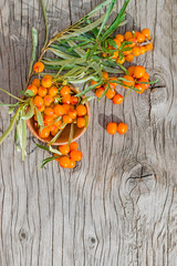 Ripe berries of the medicinal plant sea buckthorn on branches with green leaves lie in a wooden plate on a wooden table vintage, autumn harvest, copy space