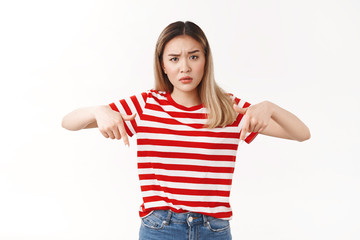 Confused clueless blond asian girlfriend frowning raise eyebrow questioned pointing down index...