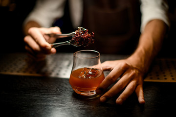 Professional bartender adding chilled melting caramel with twezzers to the cocktail glass with ice cubes